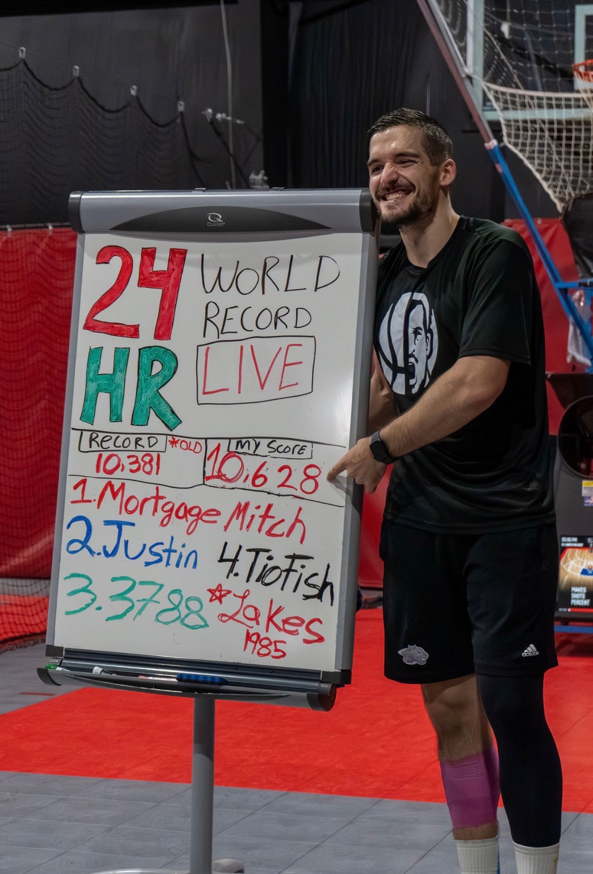 Seth McCoy next to a whiteboard showing his 24 hour basketball shooting world record score of 10,628